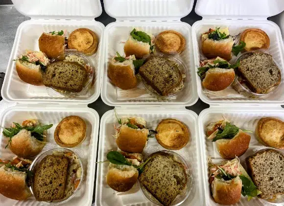 Lunch and Catering Packs A group of styrofoam containers with sandwiches and pastries